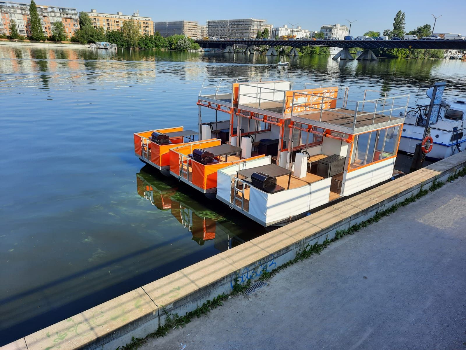 Drei orange-weiße Grillboote von Grill-Boot.de am Anleger an der Spree in Berlin